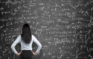 Rear view of a thoughtful woman who tries to solve math problems. Math calculations on black chalk board. Thinkstock