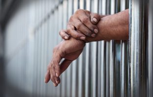 Photo of hands through prison bars