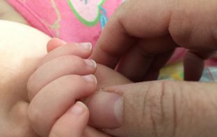 Infant and mother hold hands