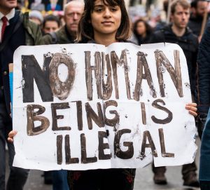 Woman holding sign saying No Human Being is Illegal