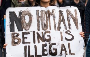 Woman holding sign saying No Human Being is Illegal