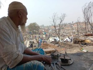 An elderly Rohingya Refugee man looks out upon the devastation caused by the fires that burned down the homes of thousands in April 2021 Photo by Mohamned Zobair