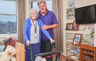 Ed Balls standing behind an elderly lady with a walker