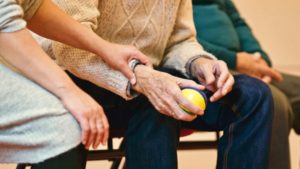 Hands of an elderly man holding a stress ball, whilst a woman comforts him