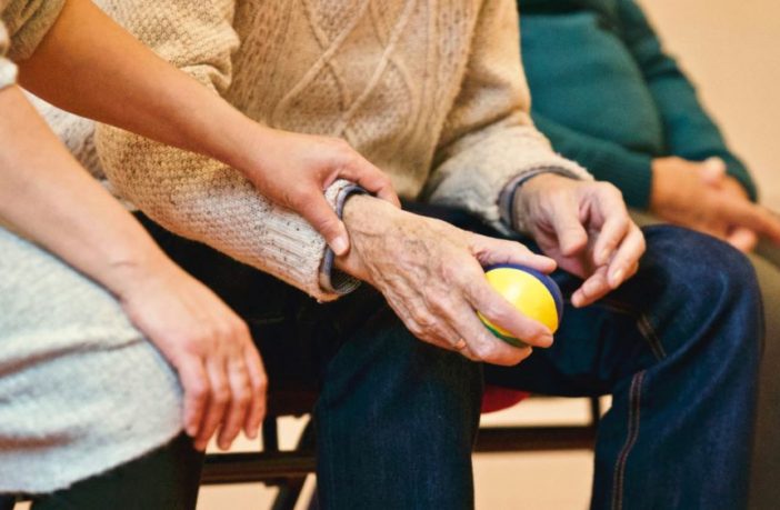 Hands of an elderly man holding a stress ball, whilst a woman comforts him