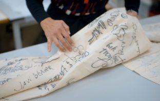 Woman's hand holding a piece of cloth with signatures written on it