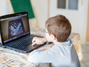 Young boy with glasses playing online chess board game on computer