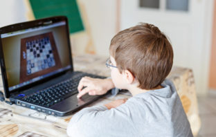 Young boy with glasses playing online chess board game on computer