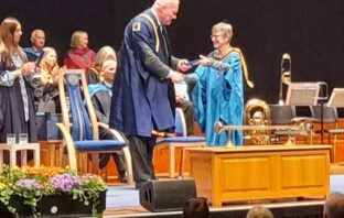 Celia shaking hands on stage while crossing the stage at the Poole graduation ceremony.