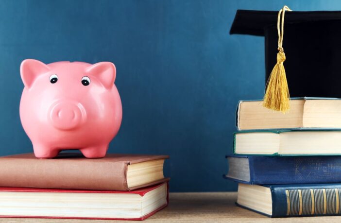 Image shows piles of books with a piggy bank and graduation cap