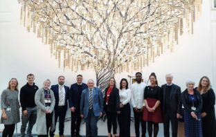 Image shows group of attendees of the OU visit standing in front of the gold tree in the university library
