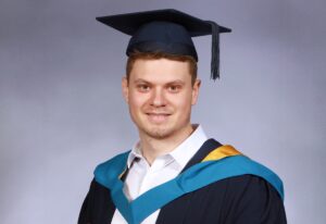 James holding his scroll wearing graduation gown and mortar, smiling at the camera.
