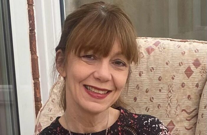 Gina sitting on the sofa, head and shoulders shot, smiling to the camera.