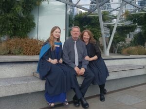 A young woman in graduation robes sat next to her smiling parents.