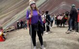 A young woman wearing walking boots and a hat in front of mountains.