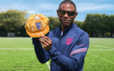 Darren Harris wearing Paralympic kit, sunglasses, facing the camera and holding a gold cap to show 100 caps for the England blind football team.