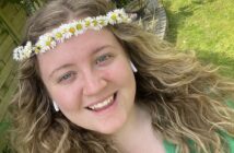 A young women with long blonde hair and a flower crown, smiles at the camera.