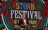 Image of a man dressed in a suit holding drum sticks on the stage at Glastonbury Festival