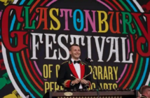 Image of a man dressed in a suit holding drum sticks on the stage at Glastonbury Festival