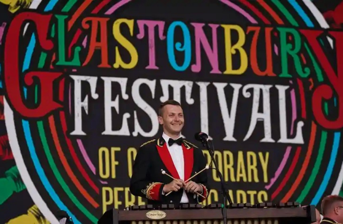 Image of a man dressed in a suit holding drum sticks on the stage at Glastonbury Festival