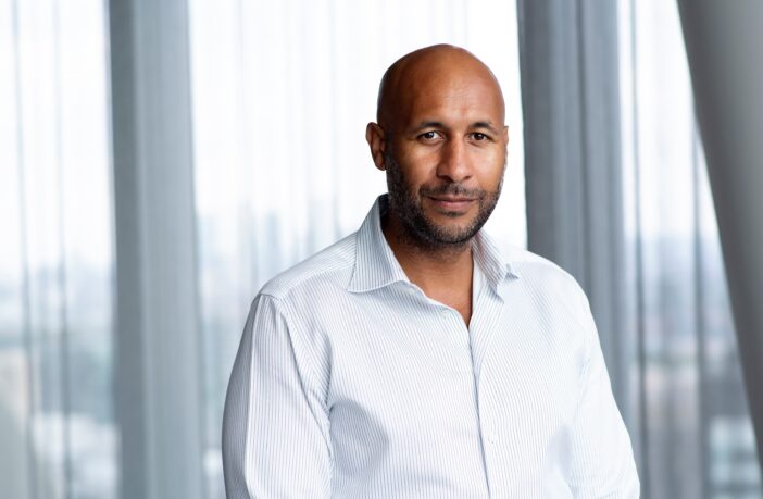 A profile shot of Thomas sitting in front of a window, dressed in a white shirt facing the camera.