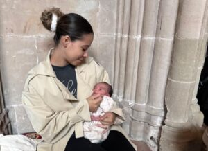 Destanhy sitting down looking at and holding her baby.