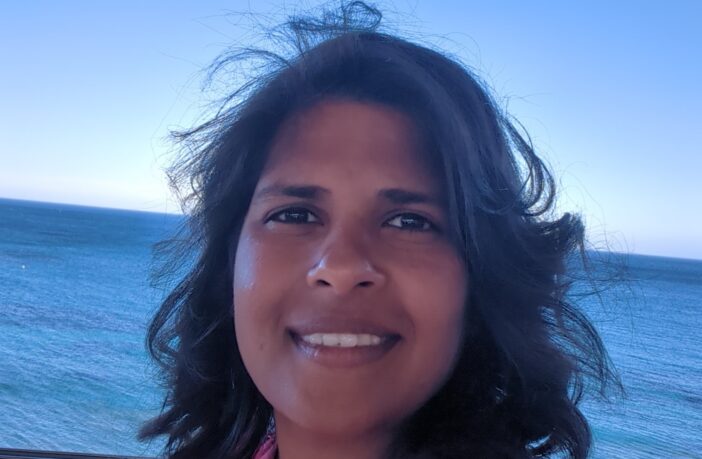 Maria smiling and facing the camera with the ocean in the background.